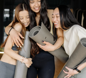 Three women hugging with yoga mats, smiling